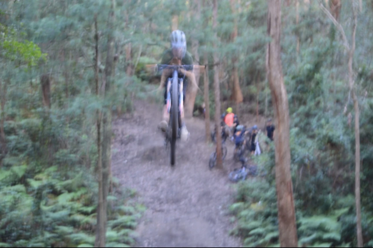 Helmeted mountain-bike rider airborne above a wooded dirt trail