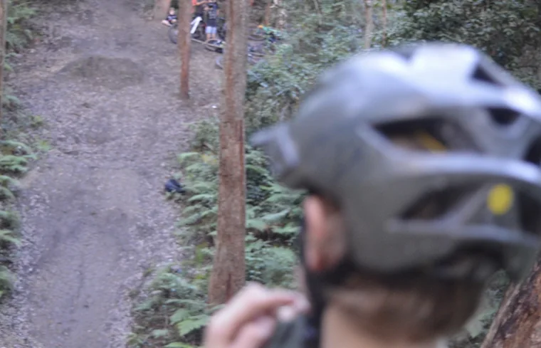 Close view of a rider wearing a black helmet beside a wooded dirt trail
