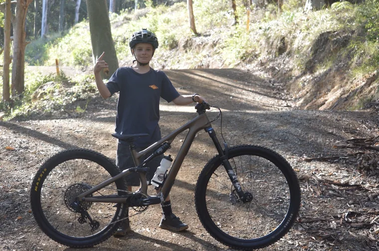Helmeted rider standing with a mountain bike on a sunlit forest trail
