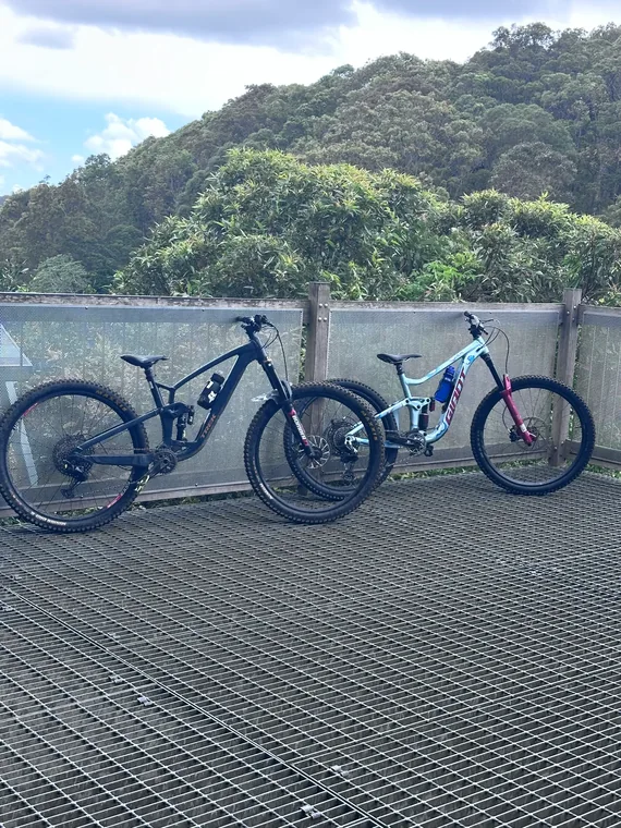 Two mountain bikes parked on a metal platform in front of forested hills and a cloudy sky